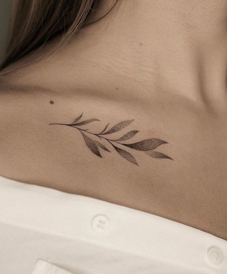 a woman's back shoulder with a small leaf tattoo on it