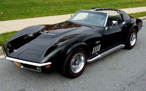 an old black sports car parked on the side of the road in front of some grass