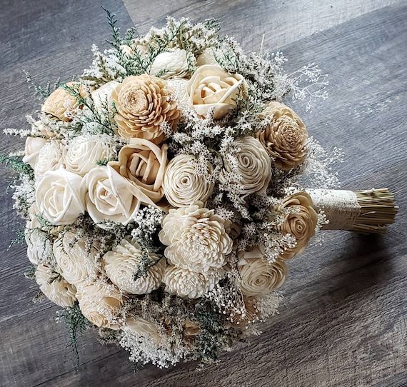 a bridal bouquet with white flowers and pine cones on a wooden table, ready to be used as a bride's bouquet