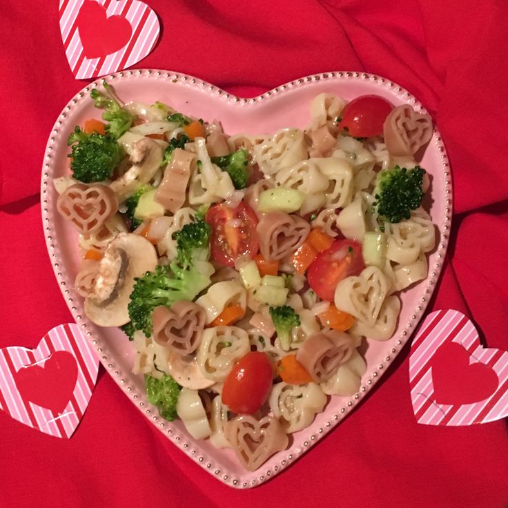 a heart shaped plate filled with pasta, broccoli and hearts on red fabric