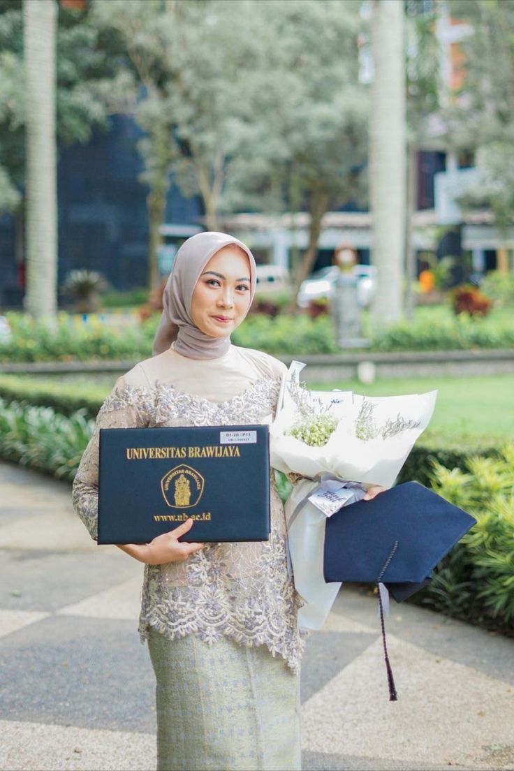 a woman in a hijab holding flowers and a diploma