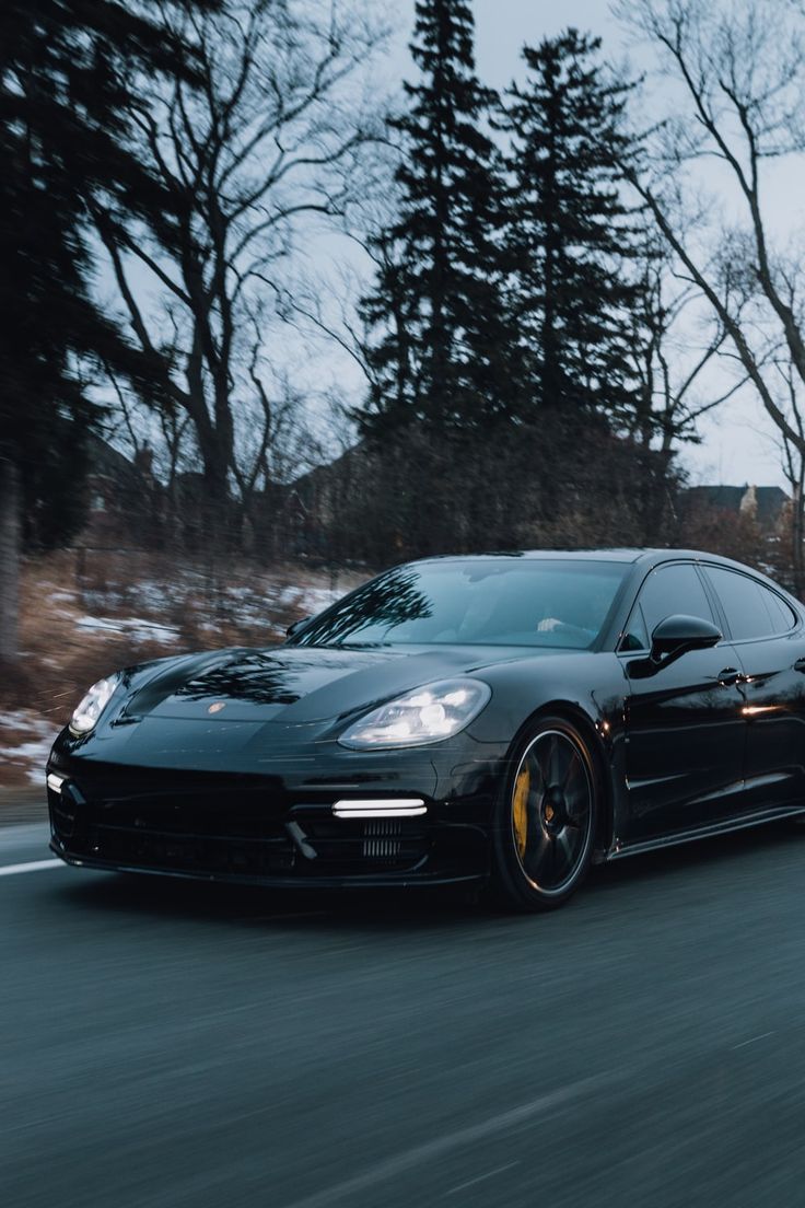 a black sports car is driving down the road in front of some snow covered trees