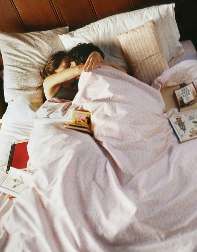 a woman laying in bed with her head on the pillow and reading books next to her