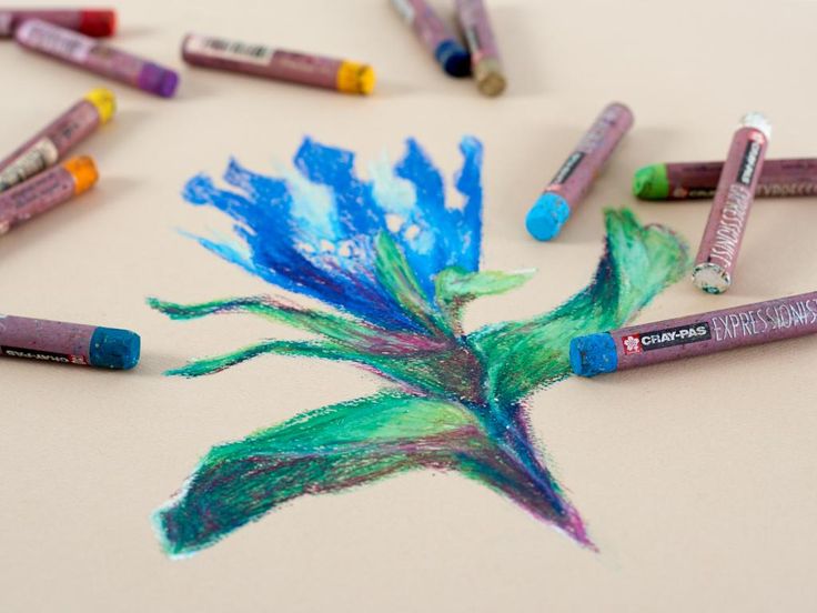 some crayons are laying on the table and there is a blue flower with green leaves