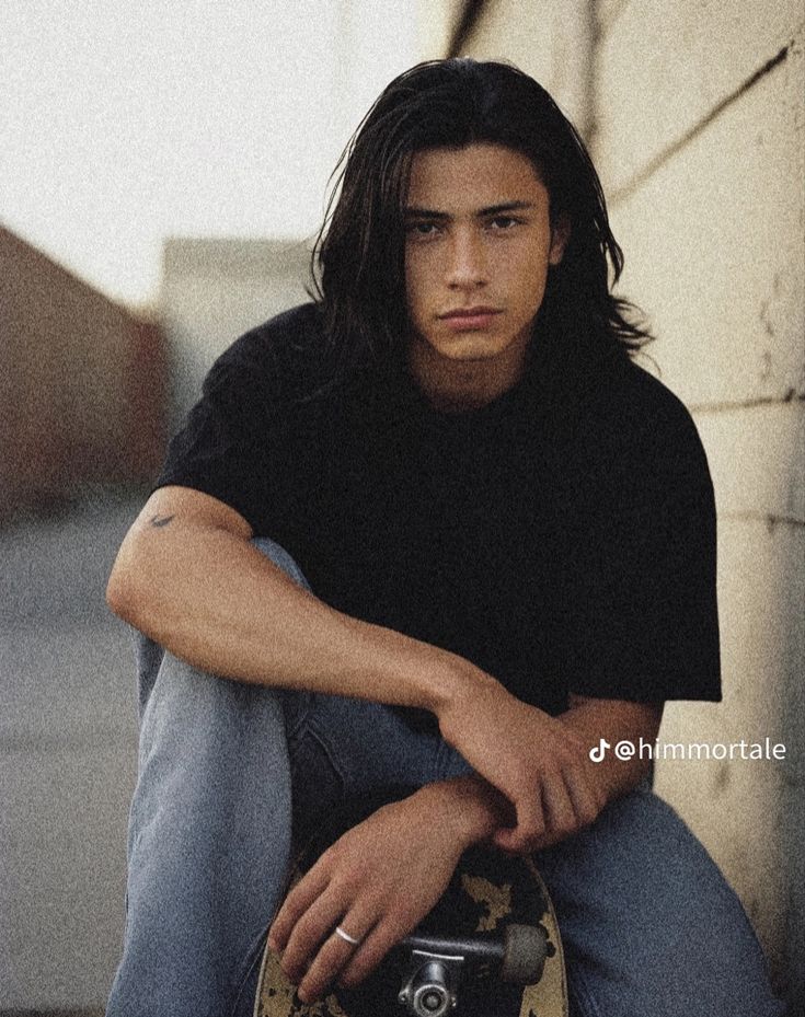 a young man sitting on the ground with his skateboard in front of him and looking at the camera