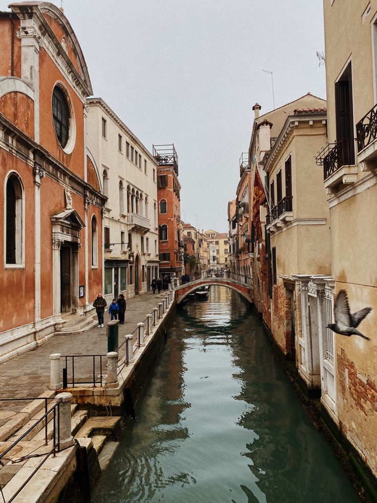 people are standing on the edge of a narrow canal in an old european city,