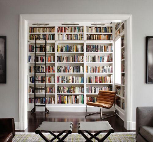 a living room filled with lots of books on top of a white book shelf next to a window