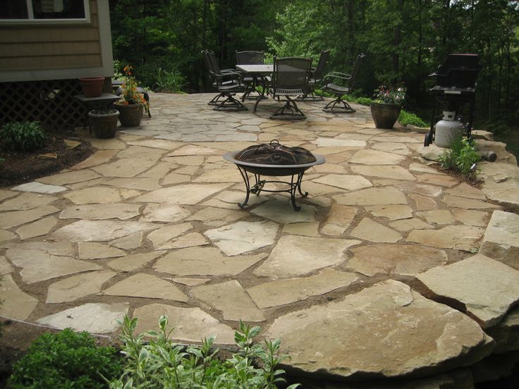 an outdoor patio with stone pavers and fire pit in the middle, surrounded by greenery