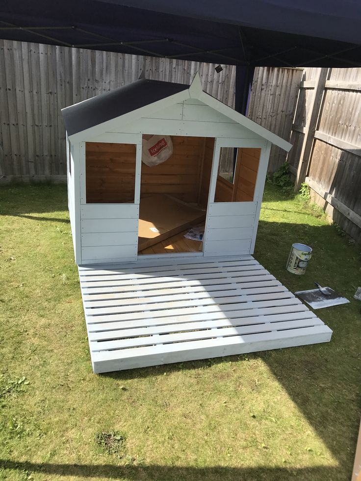 a small white shed sitting on top of a grass covered yard next to a wooden fence