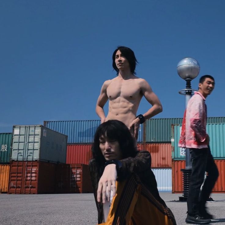 two men standing next to each other in front of shipping containers and one man with no shirt on