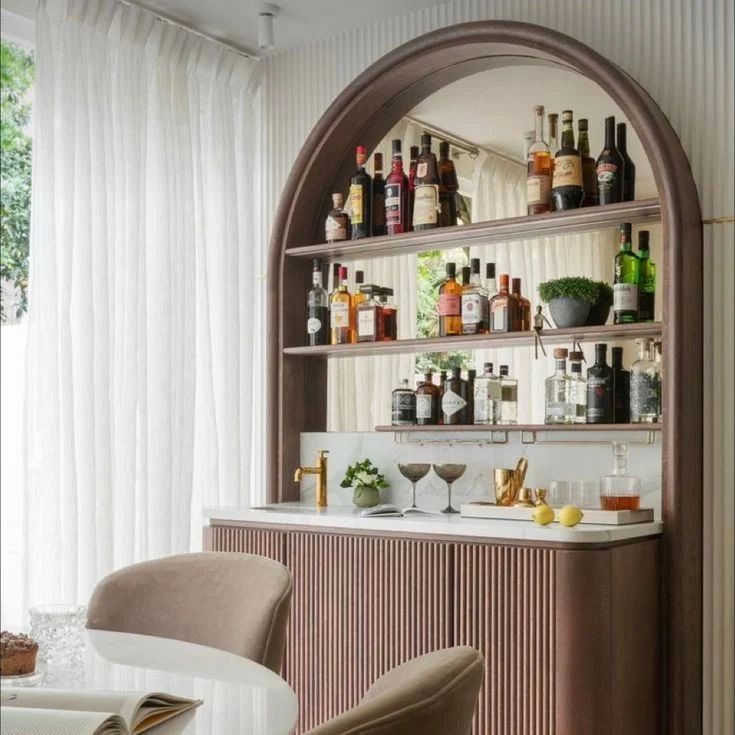 a bar with lots of bottles and glasses on the shelves above it, along with two chairs