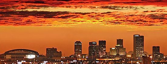 the city skyline is lit up at night with bright orange and red clouds in the sky