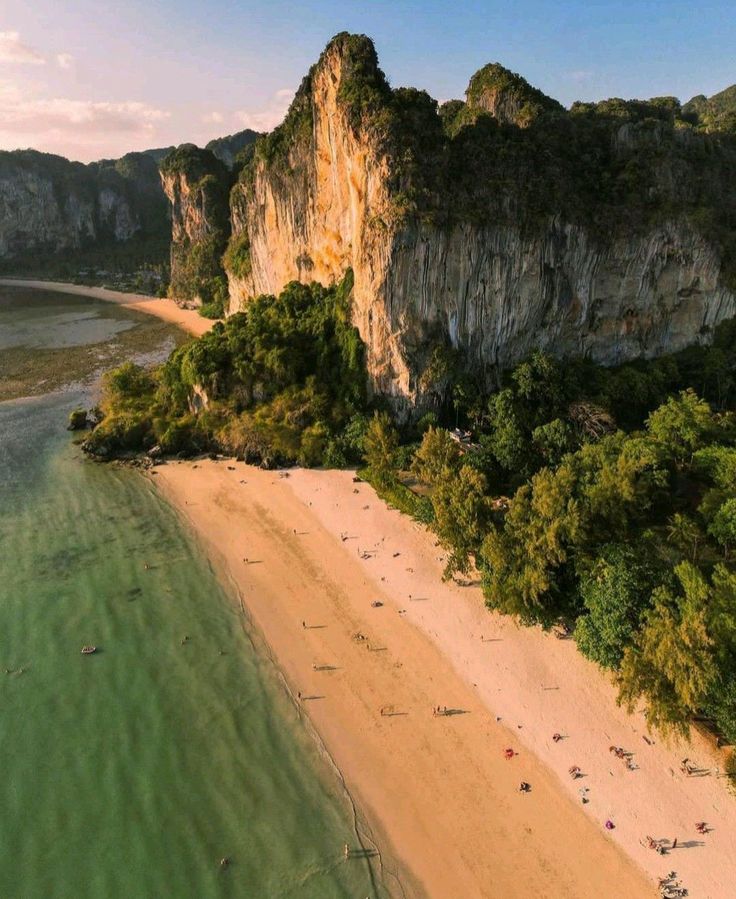 an aerial view of a sandy beach with green trees on the shore and cliffs in the background