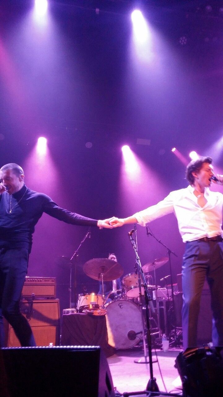 two men on stage with microphones in their hands and one man holding his arm out