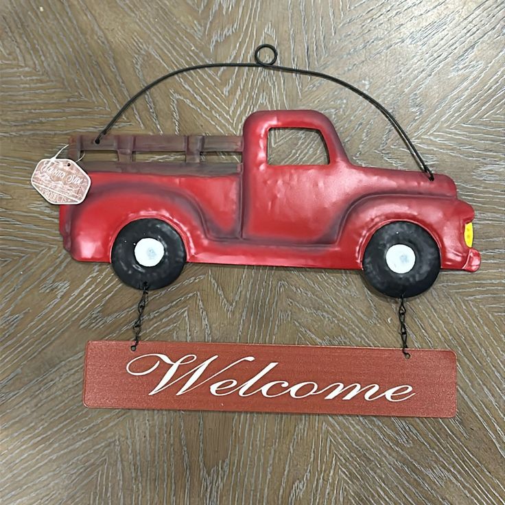 a welcome sign hanging from the side of a wooden wall with a red truck painted on it