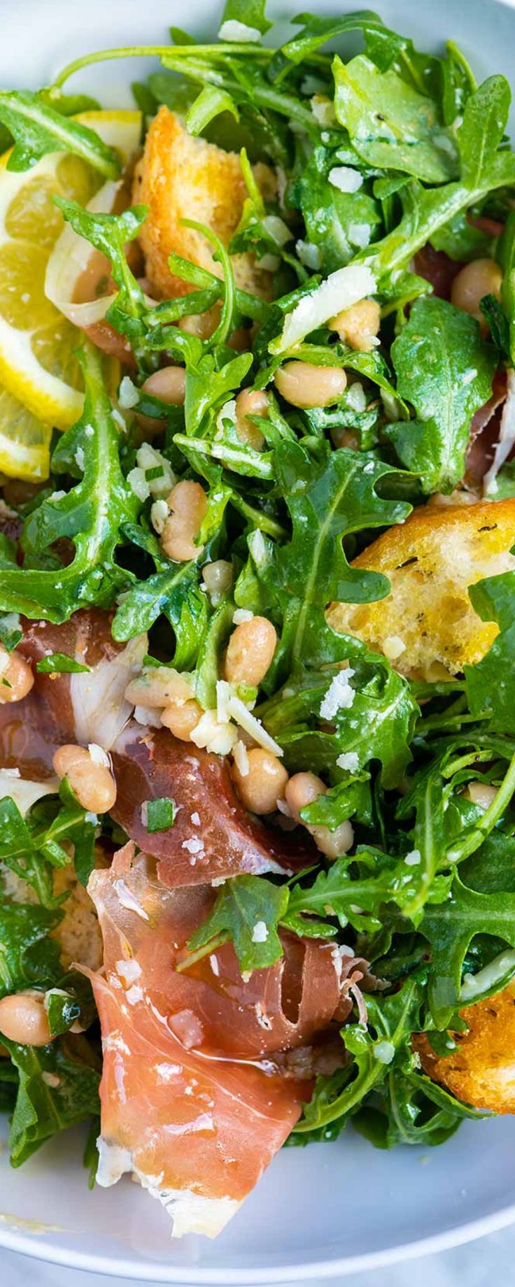 a white plate topped with salad and lots of meat on top of it's leaves