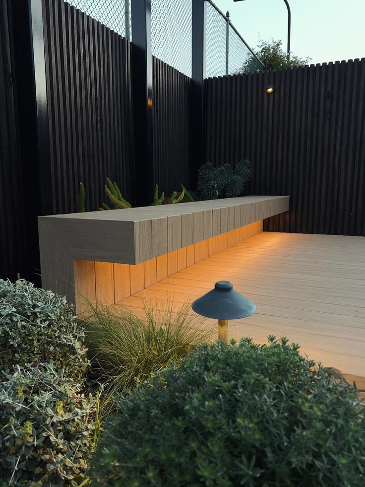 a wooden deck surrounded by bushes and plants with lights at the end on either side