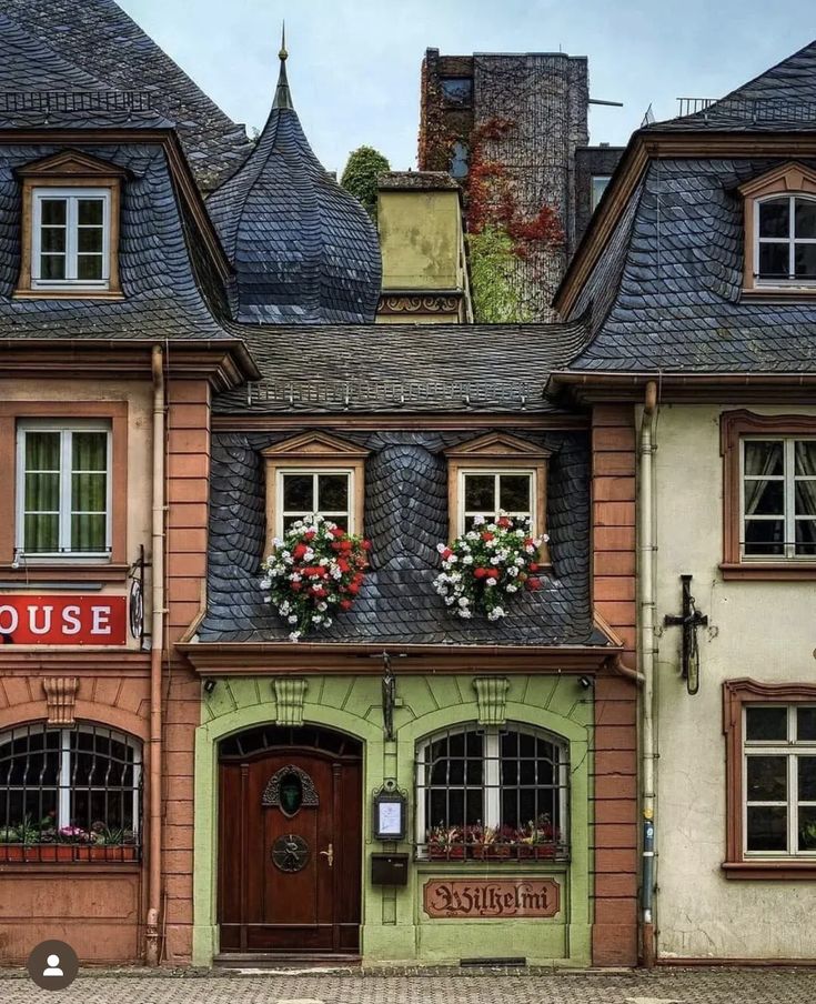 an old building with flowers on the windows and a sign above it that says house