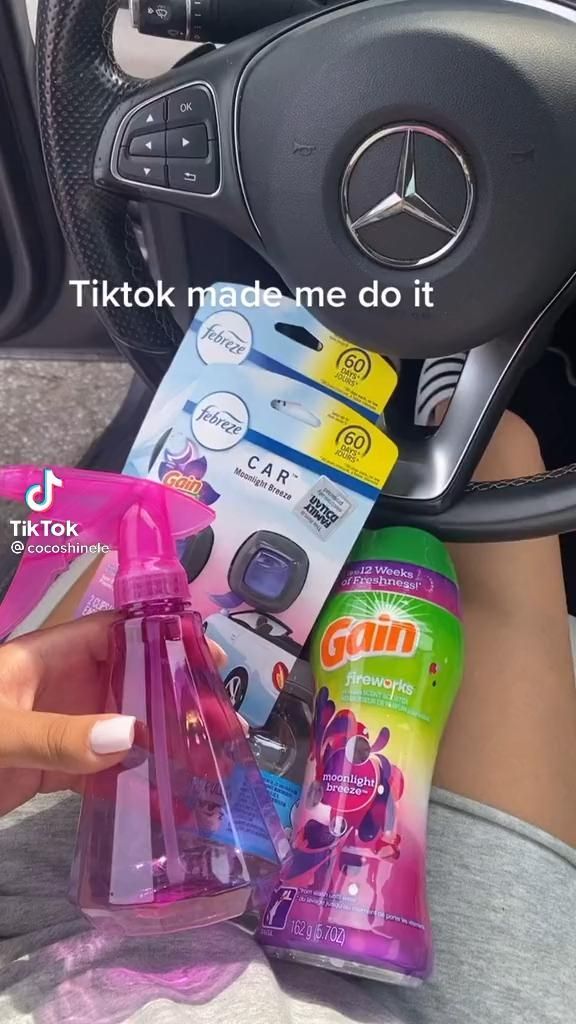 a person holding a pink bottle in their hand and cleaning the inside of her car