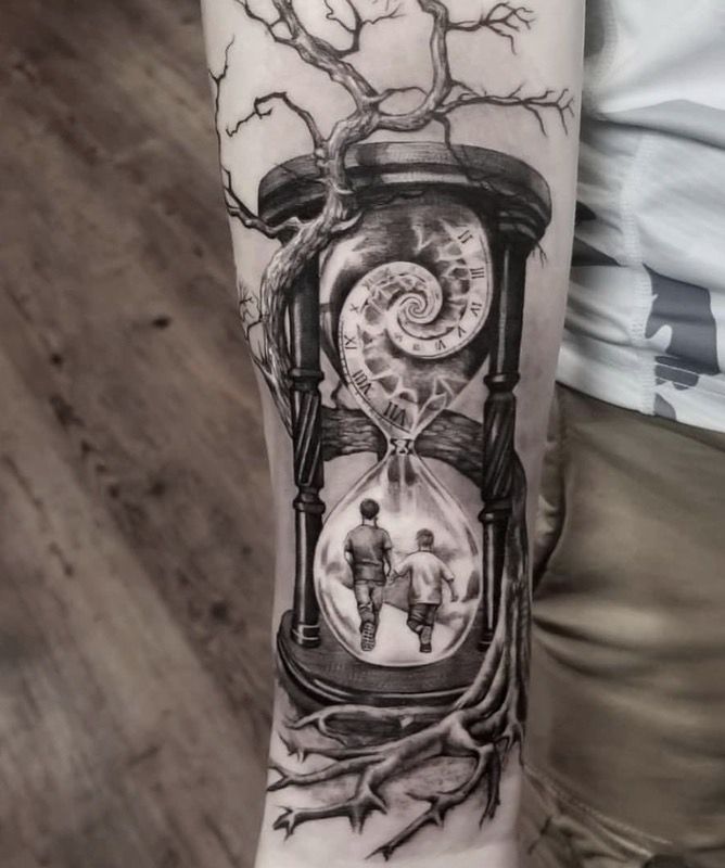 a man's arm with a clock and tree tattoo design on the left forearm