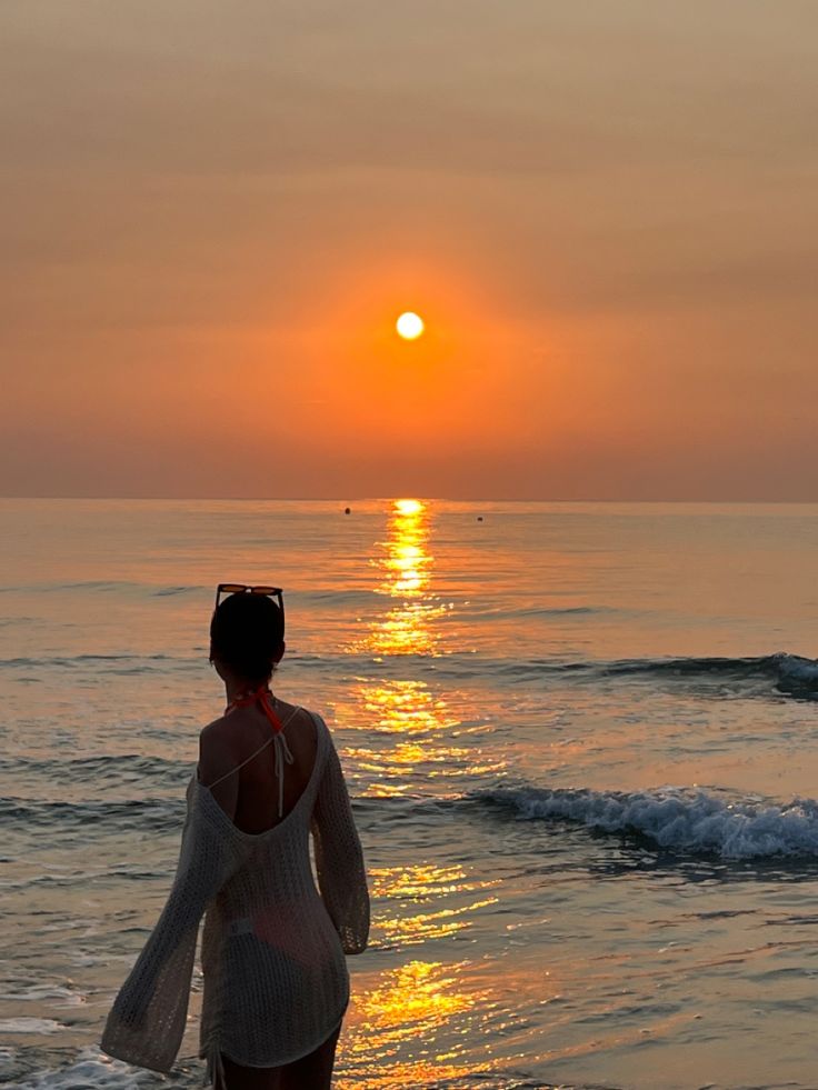 a woman walking on the beach at sunset