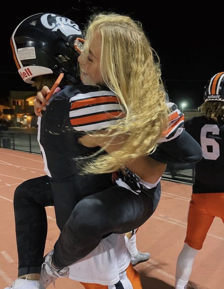 a football player is being hugged on the sidelines by another person with long blonde hair