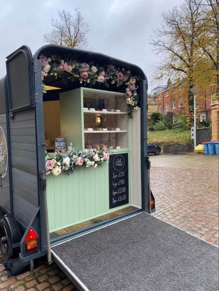 a small food truck parked on the side of a road with flowers growing out of it