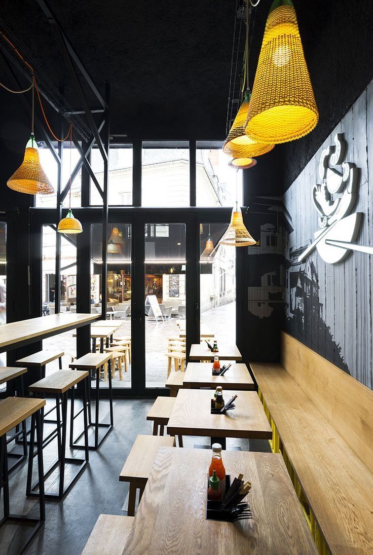 an empty restaurant with wooden tables and yellow lights hanging from the ceiling, along with black walls