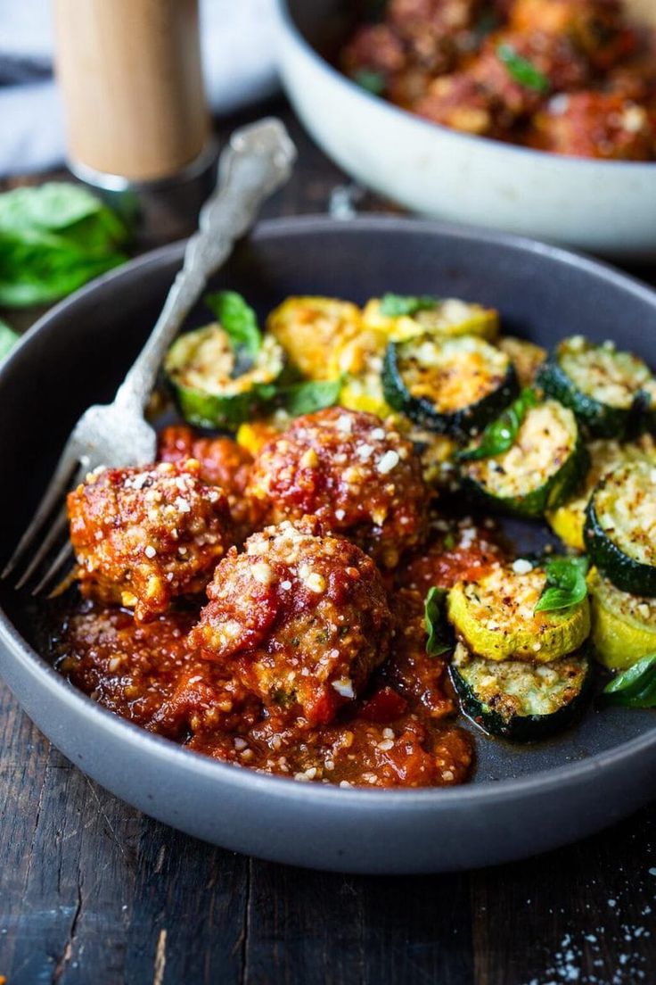 a bowl filled with meat covered in sauce next to a plate of stuffed zucchini