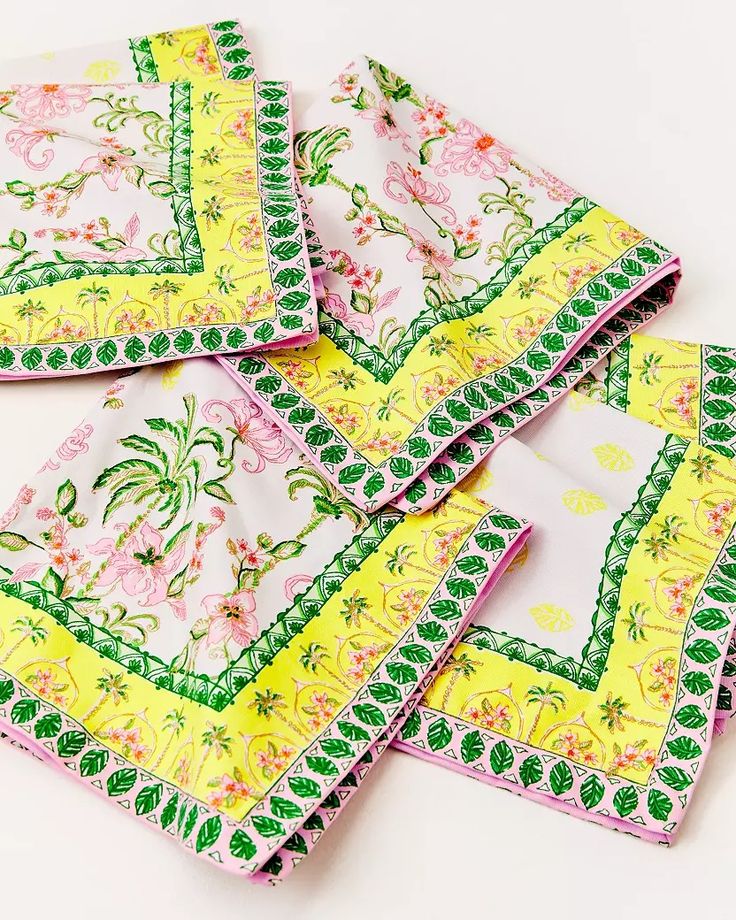 six yellow and green floral napkins on a white tablecloth with pink flowers in the center