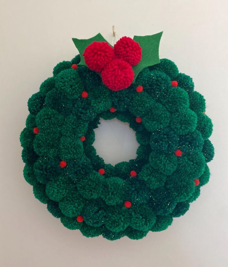 a green wreath with pom - poms hanging on the wall next to a candle