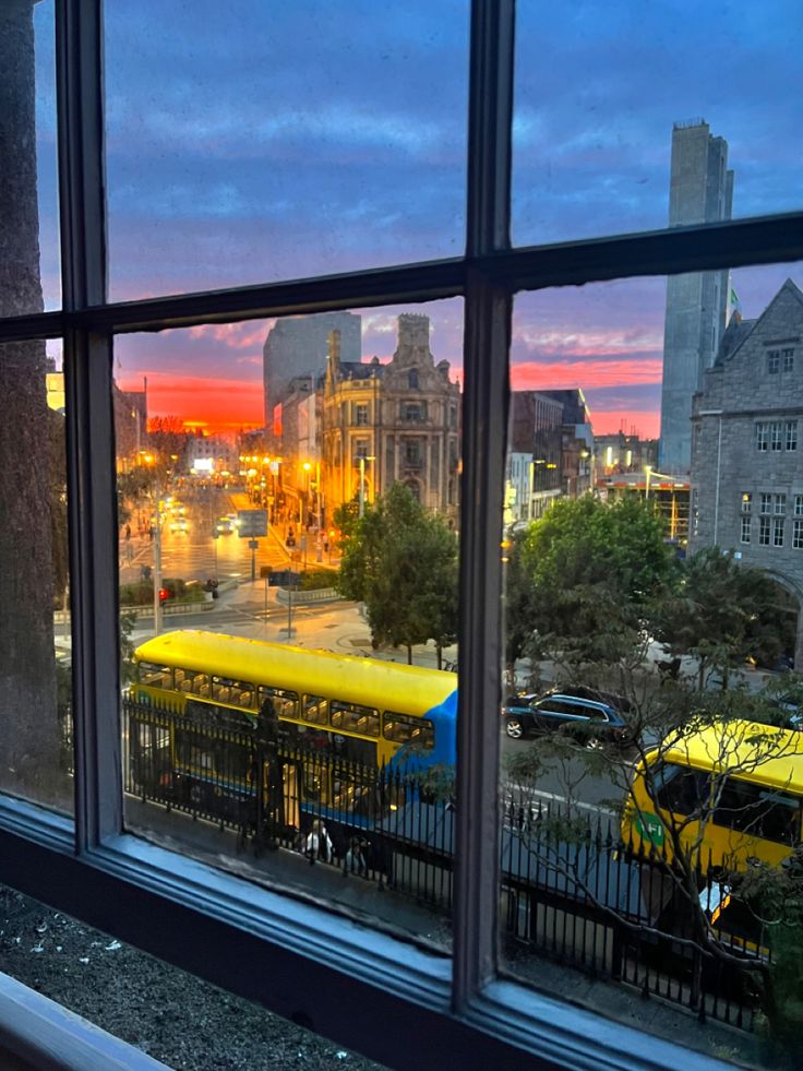 a view out the window of a bus terminal at dusk, with buildings in the background