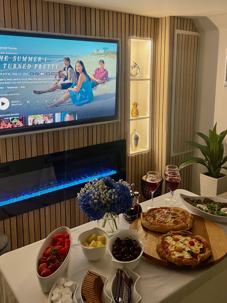 a table topped with pizzas and bowls of fruit next to a flat screen tv