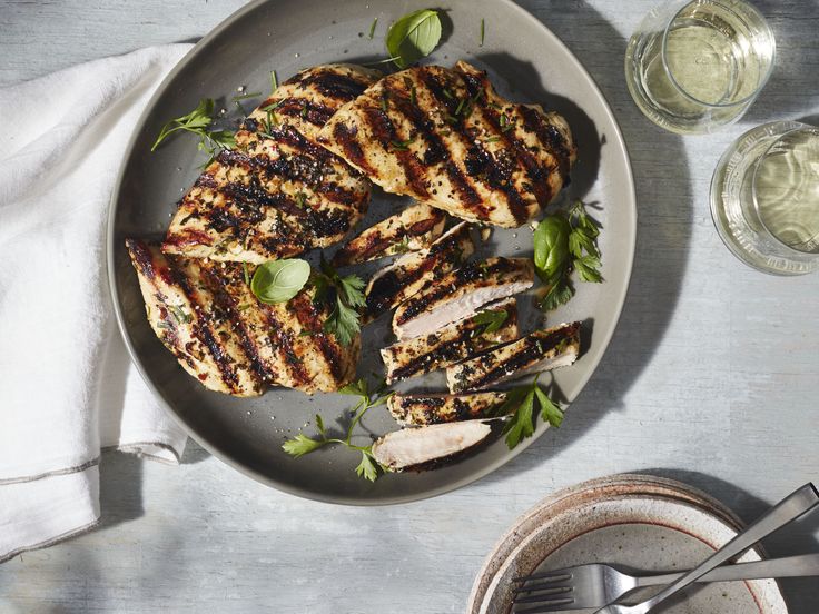 grilled chicken with herbs on a plate next to glasses of water and napkins