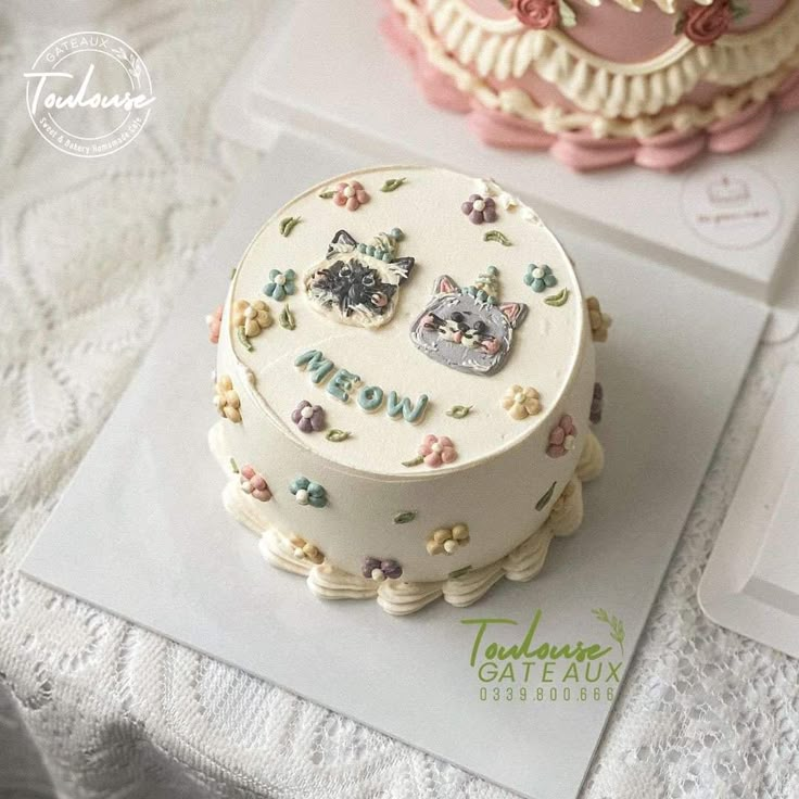 two decorated cakes sitting on top of a white table next to each other, one has a cat and the other has flowers