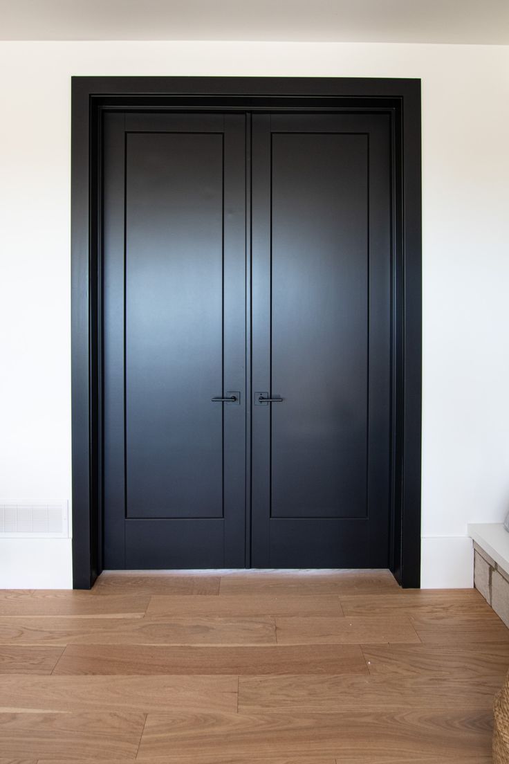 two black doors in the corner of a room with hardwood floors and white walls,