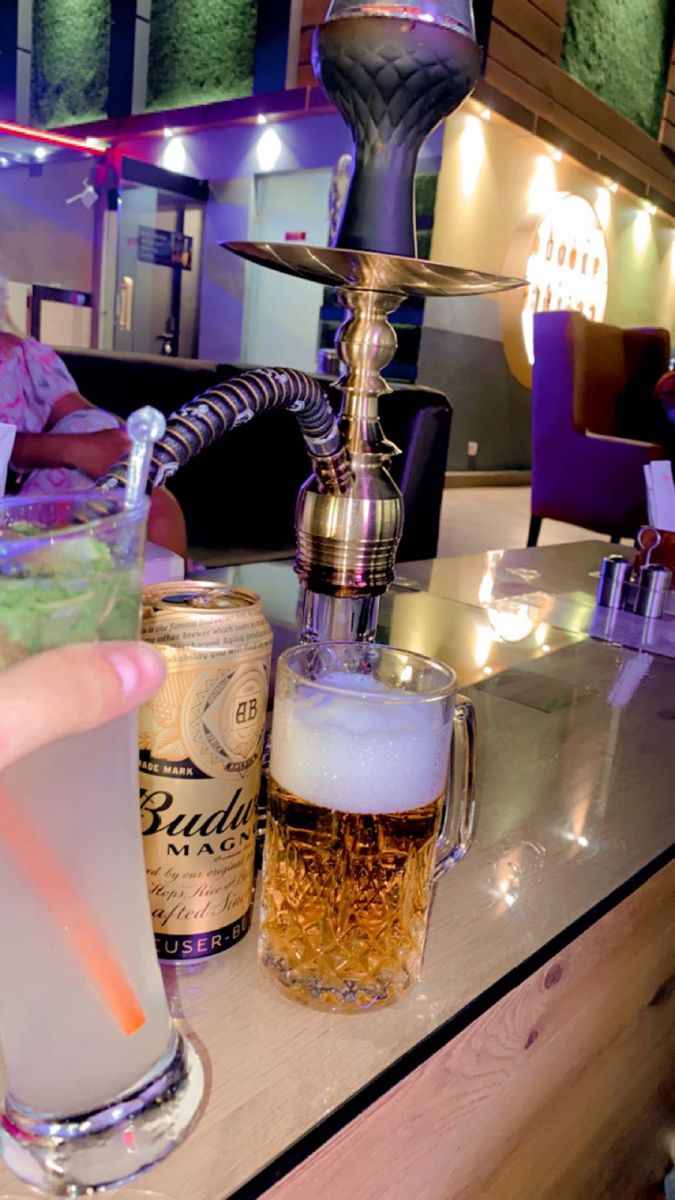 a person is holding a drink in front of some drinks on a bar counter with people sitting around