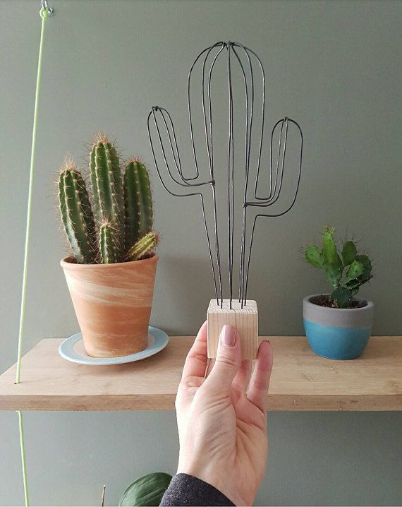 a person is holding up a wire cactus plant holder