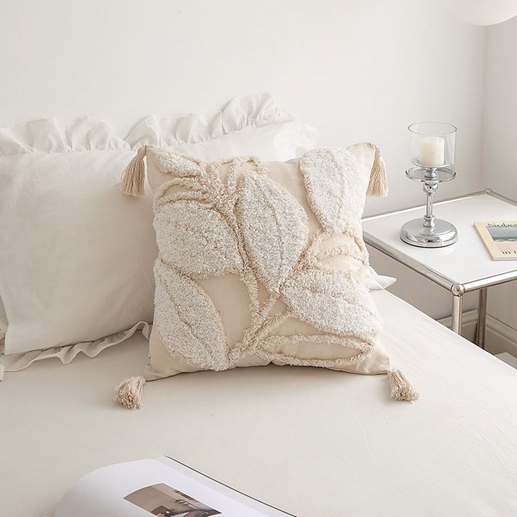 a white bed topped with pillows next to a night stand and table filled with books