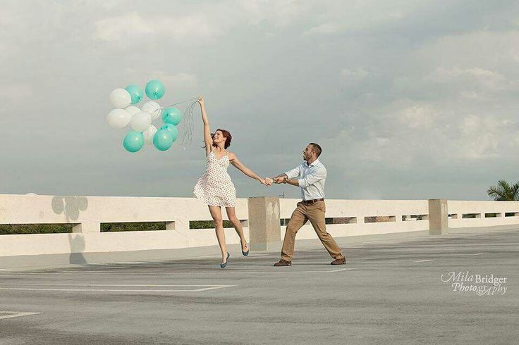 a man and woman holding balloons while walking across a parking lot with their arms in the air