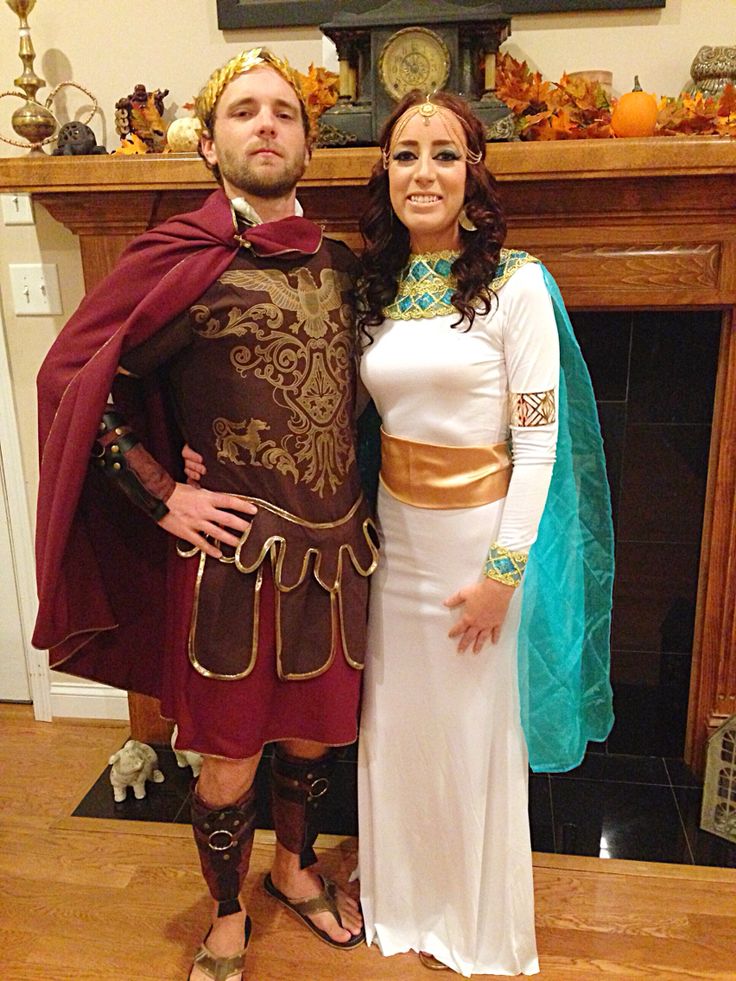 a man and woman dressed up in roman costumes posing for a photo with a fireplace behind them