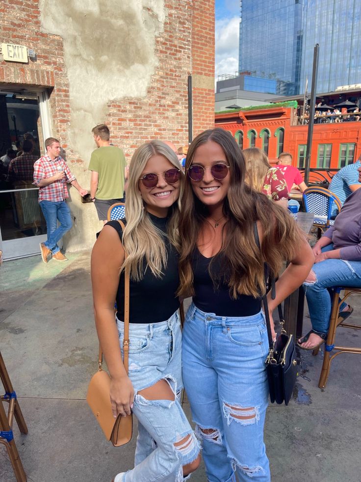 two women standing next to each other wearing ripped jeans and black tops, one with her arm around the other's shoulder