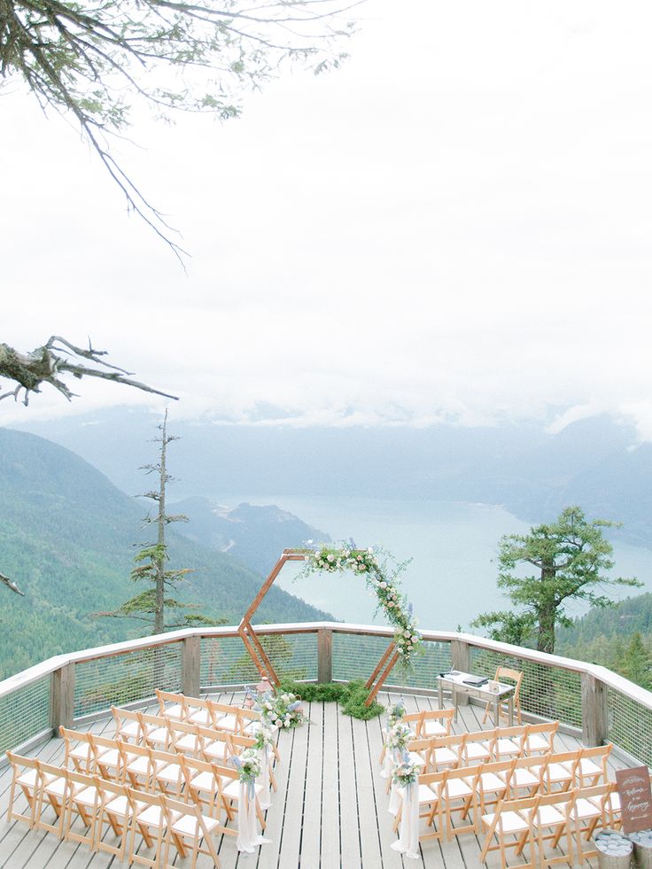 an outdoor ceremony setup with wooden chairs and greenery on the top of a mountain