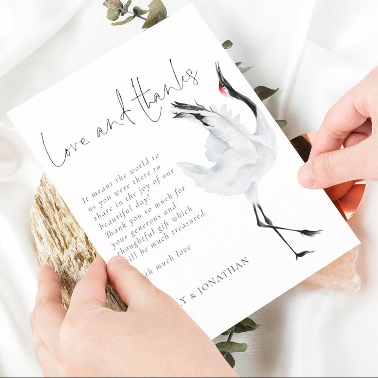 two hands holding a card that reads love and thanks with a crane on it, while another hand holds a piece of wood