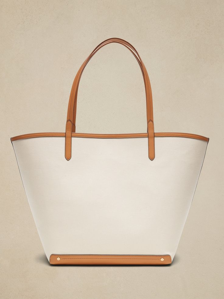 An elegant companion to everyday style, this classic tote goes anywhere with ease with spacious storage, sturdy leather trim, and a snap closure.  Sturdy leather handles.  Open top with snap closure.  Height: 16" (41cm) Width: 25" (63cm) Depth: 8" (2 Canvas Leather Tote, Leather Handles, Open Top, Canvas Leather, Everyday Style, Michael Kors Jet Set, Leather Handle, Leather Trims, Leather Tote