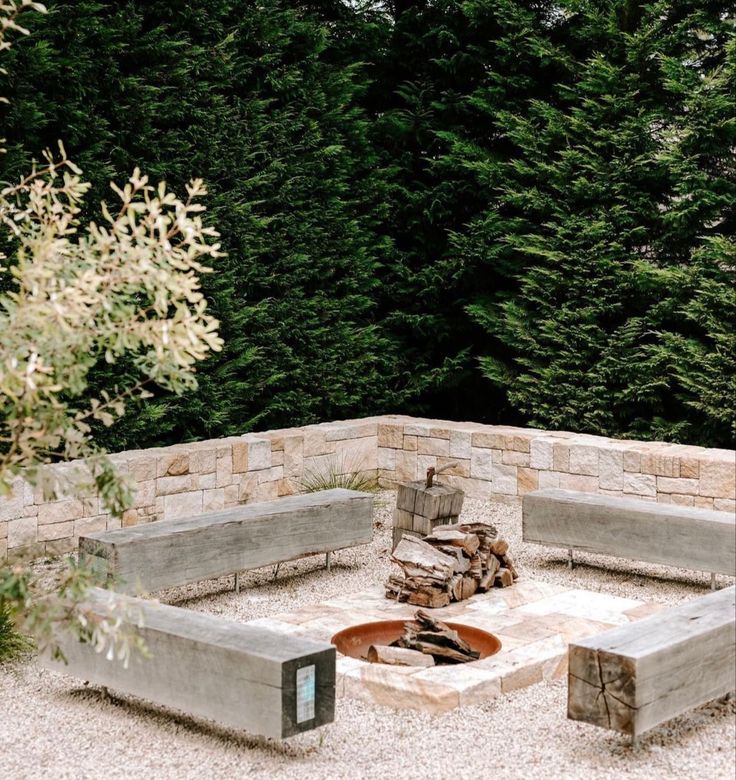 an outdoor fire pit surrounded by stone walls and benches with trees in the back ground