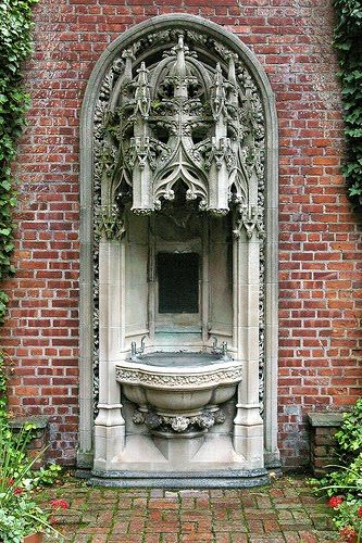 an ornate fountain in the middle of a brick wall with ivy growing on it's sides