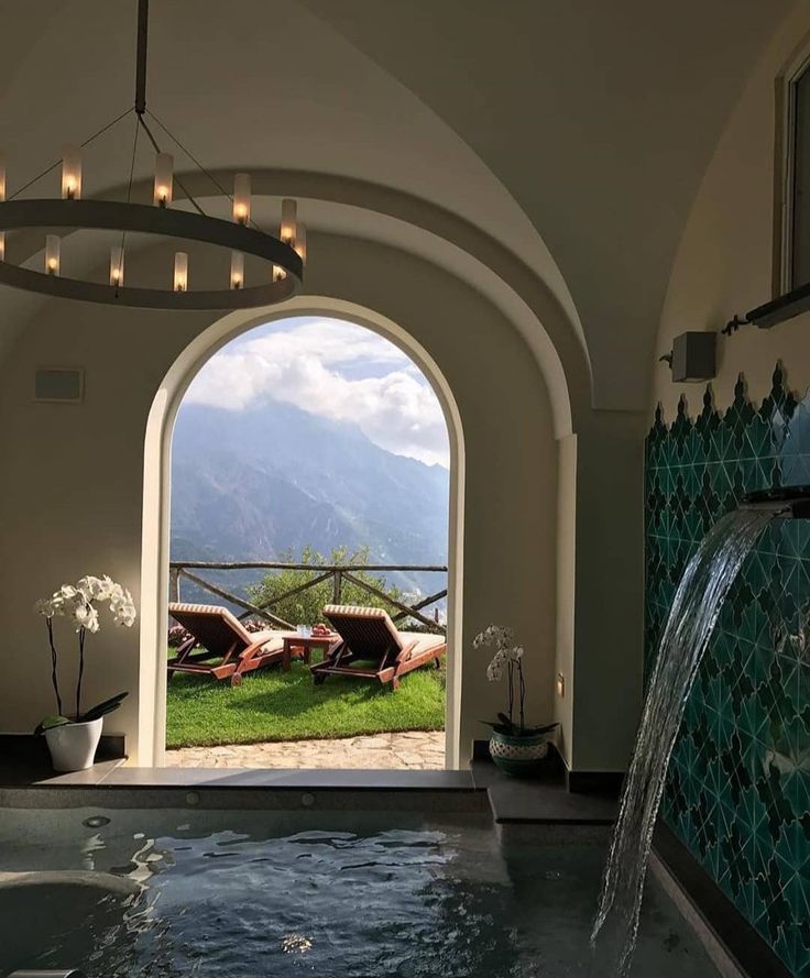 an indoor swimming pool with two chaise lounges and a waterfall in the middle