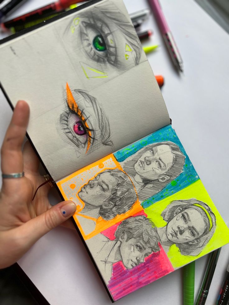 a person holding up a book with drawings on it and colored pencils next to it