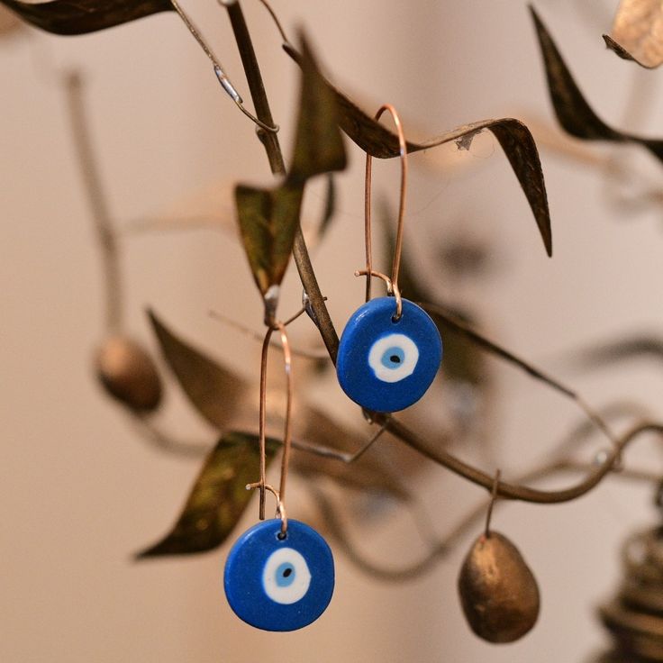 two blue evil eye earrings hanging from a tree branch with leaves and bells attached to it